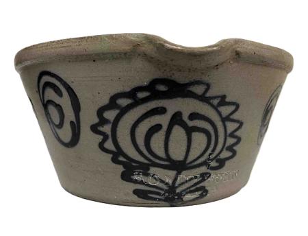 The grey salt-glazed stoneware milk pan, with sloping sides and a pour spout, is decorated with slip-trailed cobalt. The central motif is of a tulip within a sunflower. The vessel is stamped B.C.MILBURN / ALEXA.