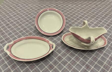 These pieces of a set of toy dishes, cream-colored with a pink rim, include a platter, plate, and gravy boat with stand.