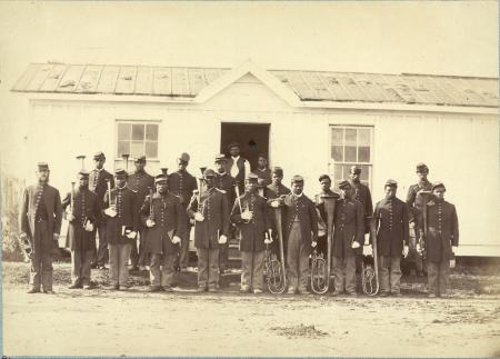 African American soldiers pose with their instruments in front of a long white building.
