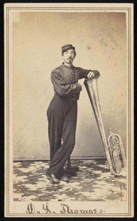 A soldier poses leaning on the bell of his large brass instrument.