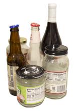 A photo of various glass items (jars with labels, bottles with caps) that can be placed in glass recycling bins. Se accompanying text for list of acceptable materials.