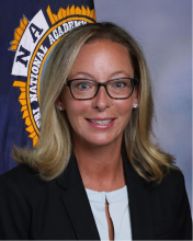 Headshot of Lt. Tara may with FBI national academy flag behind her. 