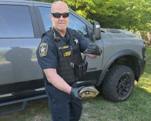 Sheriffs Deputy stands outside in front of a truck while holding a turtle
