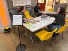 three city employees sitting on a table, four yellow chairs
